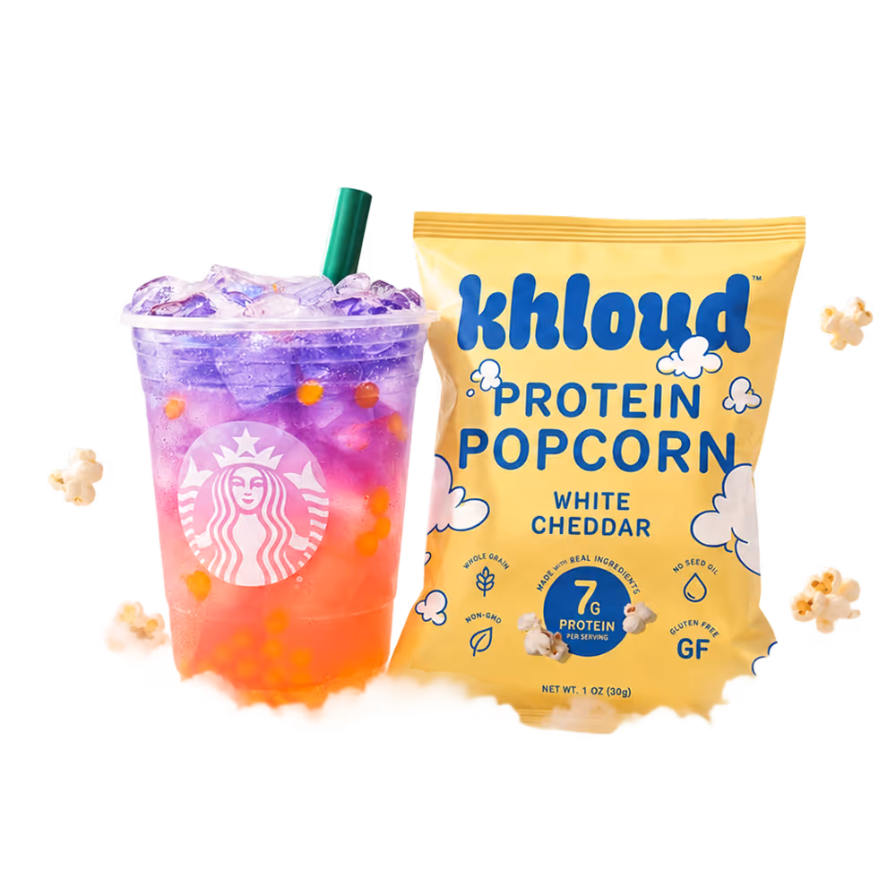 Starbucks Butterfly refresher drink sitting on a cloud in the sky next to Khloud Protein Popcorn White Cheddar in a 1oz bag, surrounded by floating pieces of popcorn